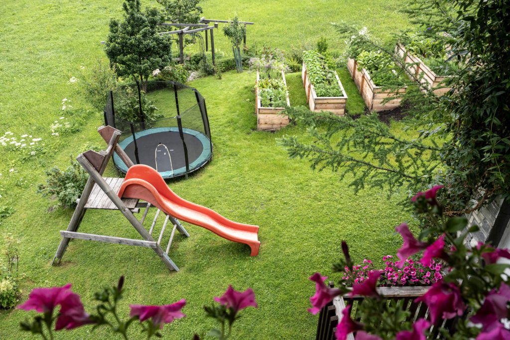 Playground with slide and trampoline, surrounded by garden beds in Hotel Lärchenhof.
