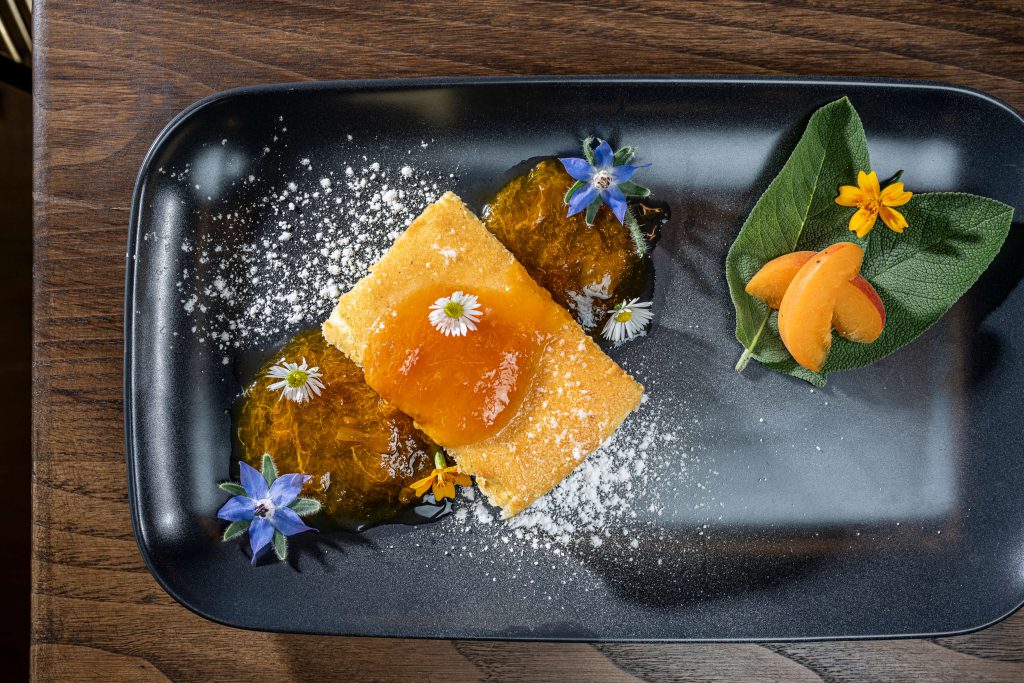 Delicious dessert with fruit, blossoms and powdered sugar on a black plate in the Lärchenhof.