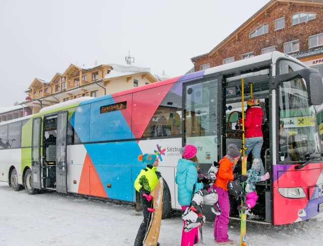 Bunte Postbusse transportieren Reisende im verschneiten Salzburger Land.